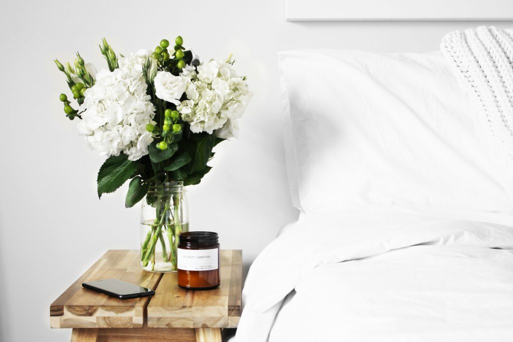 flowers-on-a-wooden-bedside-table-next-to-white-bed